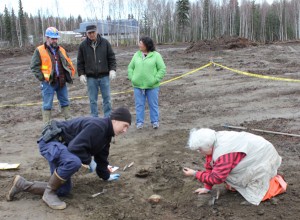 Photo by Kevin Whitworth, MTNT, Limited.. Alaska State Trooper Jack LeBlanc and forensic archaeologist Joan Dale, both on their knees, unearth part of a human skull in McGrath. Standing in the background, with the McGrath School behind them, are, from left, Brant Dallas, Lucky Egress and Betty Magnuson.