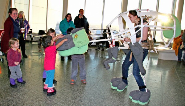  Photo by Theresa Bakker. Museum animator Hannah Foss introduces the dinosaur costume known as Snaps to the community at the open house in January. The final version will have ridged skin with scales and a crest of feathers.