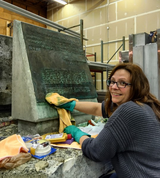 Photo by Kevin May. Senior collections manager Angela Linn wipes away corrosion from the surface of the historical plaque added to the UAF cornerstone in 1962.