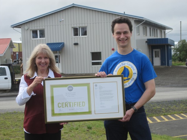 Debi McLean, director of the UAF Bristol Bay Campus in Dillingham, and Tom Marsik, assistant professor of sustainable energy, hold the Applied Sciences Center's LEED certificate from the U.S Green Building Council on Aug. 17. The center is in the background.