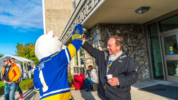 UAF photo by Todd Paris.  Interim Chancellor Mike Powers high-fives Nook the mascot outside the Moore-Bartlett-Skarland dormitory complex.
