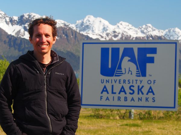 Photo by Claudine Hauri.  Andrew McDonnell poses by the UAF sign at the Seward Marine Center.