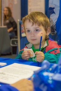 Four-year-old Oscar Misel stops by the UAF information booth to pick up a sticker and a pencil during his visit during UAF Day at the Tanana Valley State Fair.
